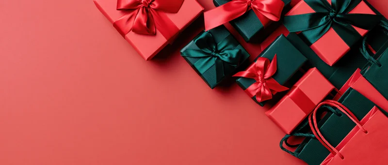 Red and dark green gift boxes with satin ribbons arranged diagonally on a red surface with copyspace
