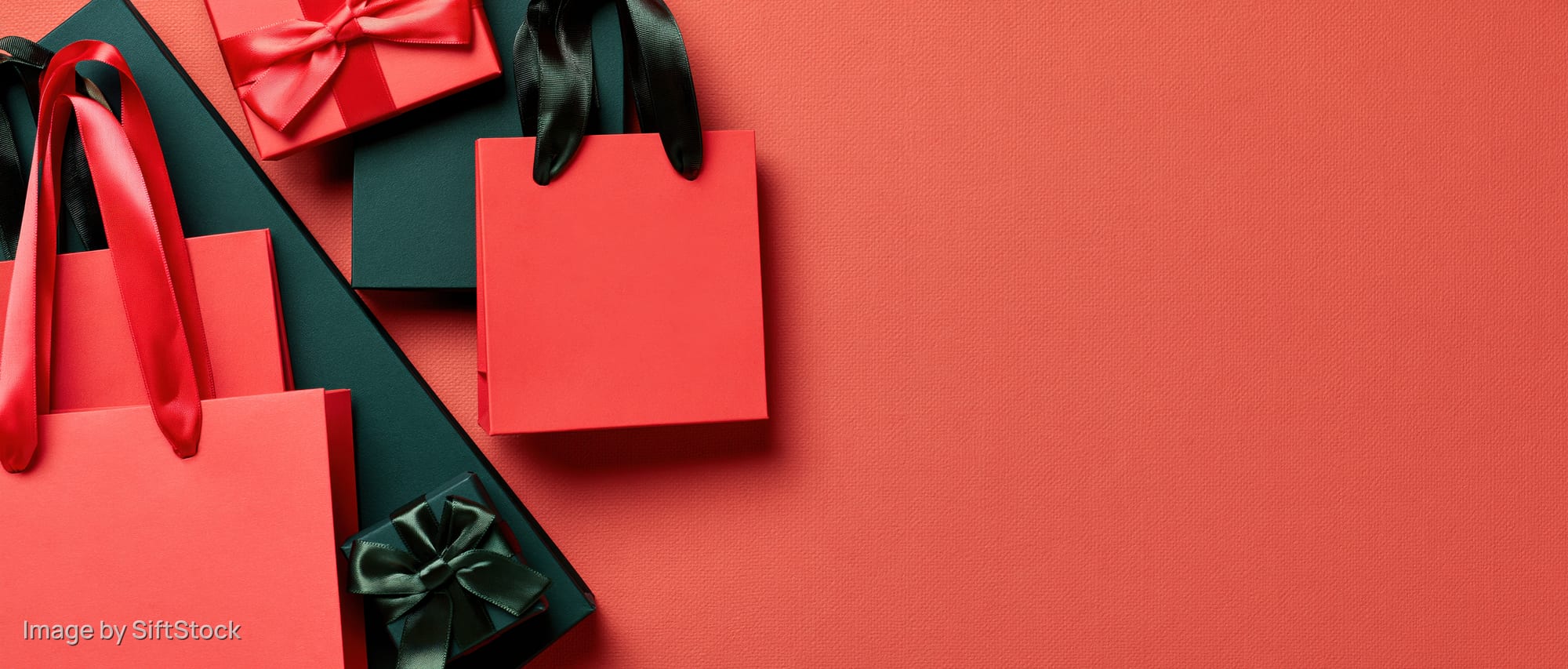 Red and dark green paper shopping bags with satin ribbons arranged in flat lay on textured surface with copyspace
