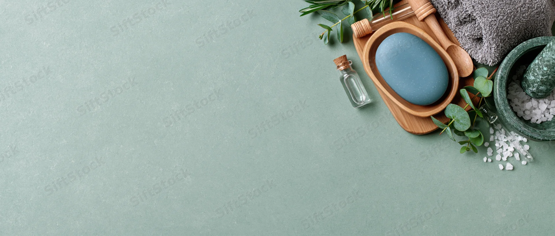 Spa and skincare items arranged on a textured green surface with copyspace on the left