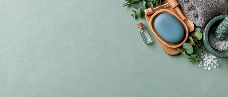 Spa and skincare items arranged on a textured green surface with copyspace on the left
