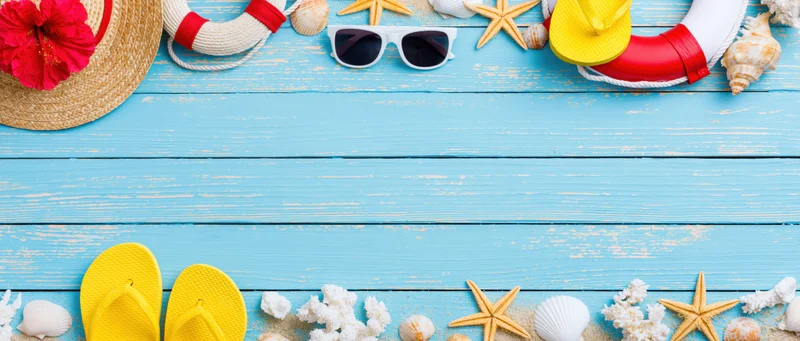 Summer beach accessories arranged along top and bottom edges of blue wooden surface with copyspace in center