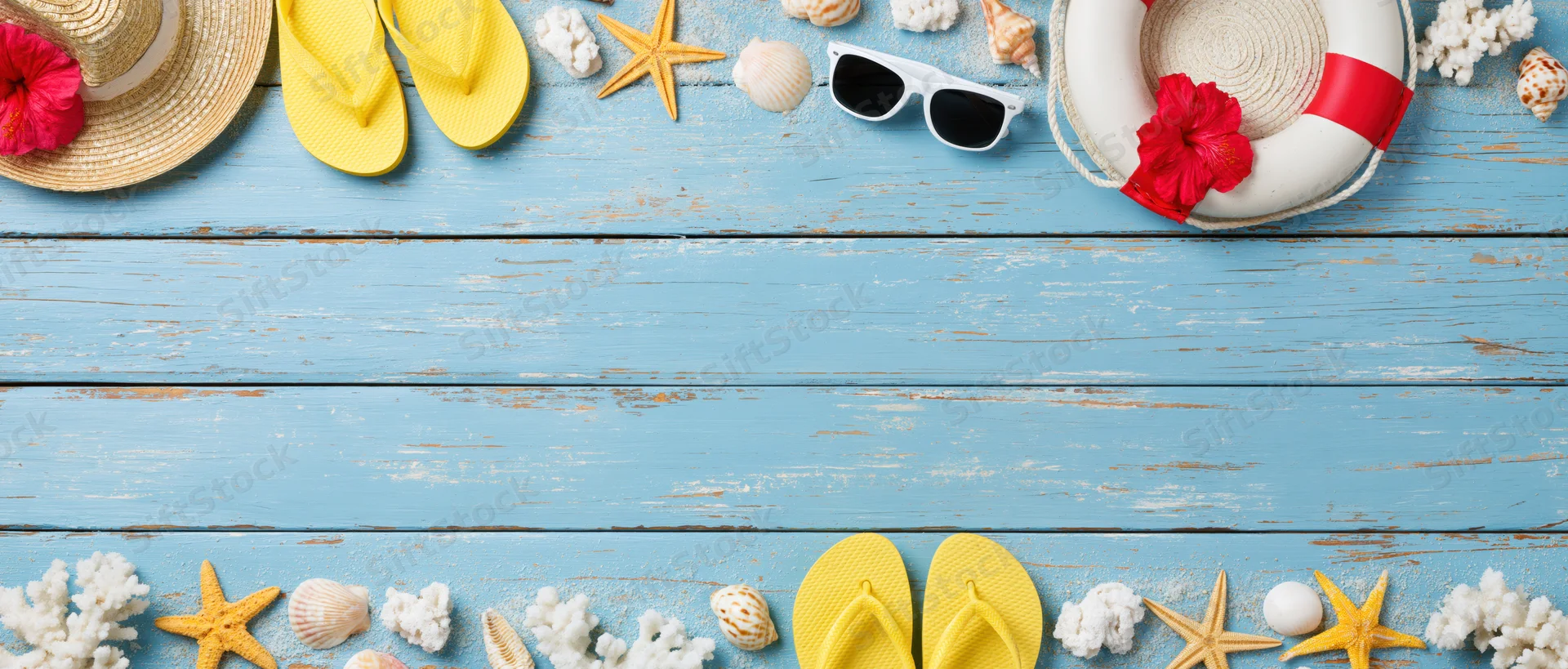 Summer beach accessories arranged along top and bottom edges of blue wooden surface