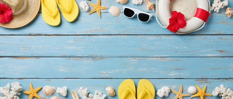 Summer beach accessories arranged along top and bottom edges of blue wooden surface