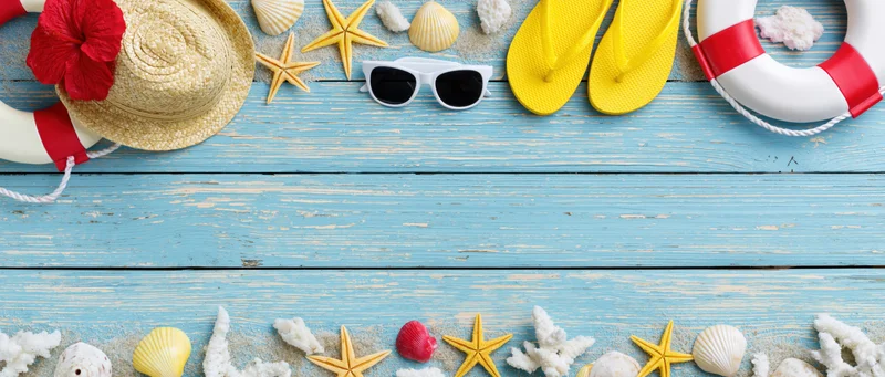 Summer beach accessories arranged along top and bottom edges of blue wooden deck