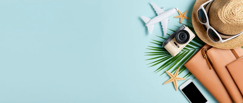 Summer travel accessories arranged on light blue background with copyspace