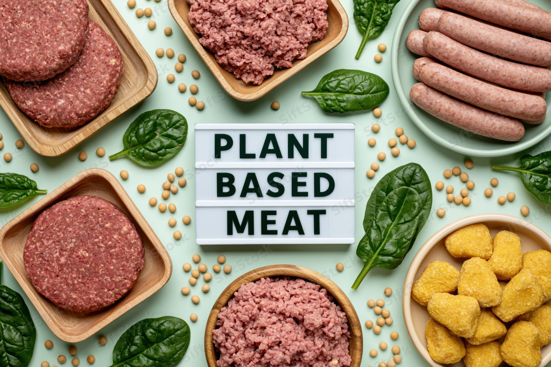 Plant-based meat products arranged in bowls and trays with soybeans and spinach on a light green surface