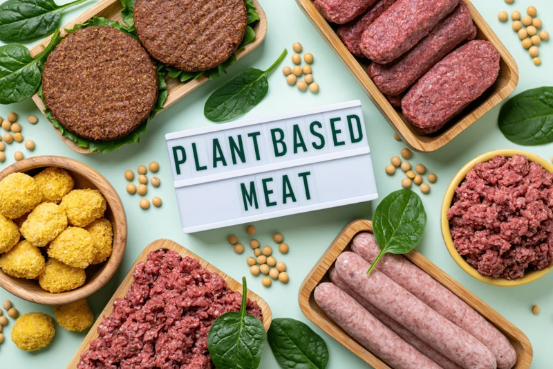 Plant-based meat products arranged in wooden trays and bowls with soybeans and spinach on a light green surface