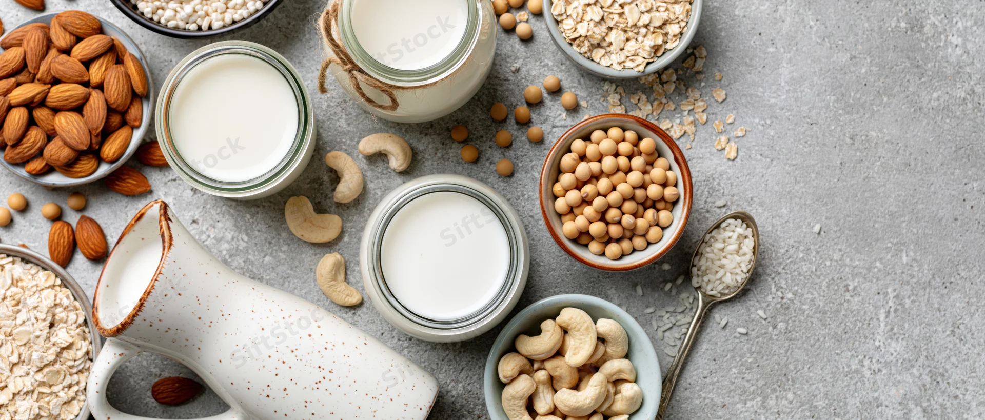 Plant-based milk alternatives in glass jars and bowls with nuts and grains on a gray countertop