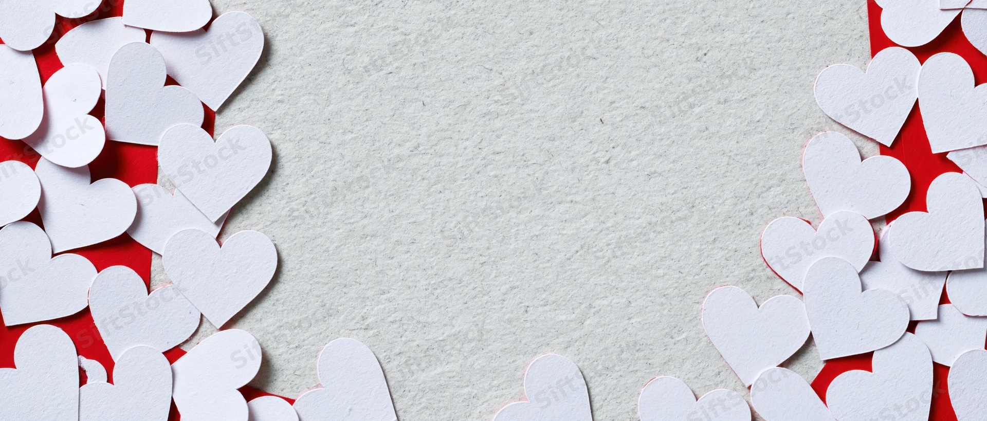 White paper heart cutouts arranged along edges of textured surface with central copyspace