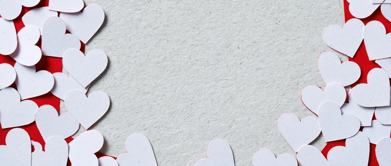 White paper heart cutouts arranged along edges of textured surface with central copyspace