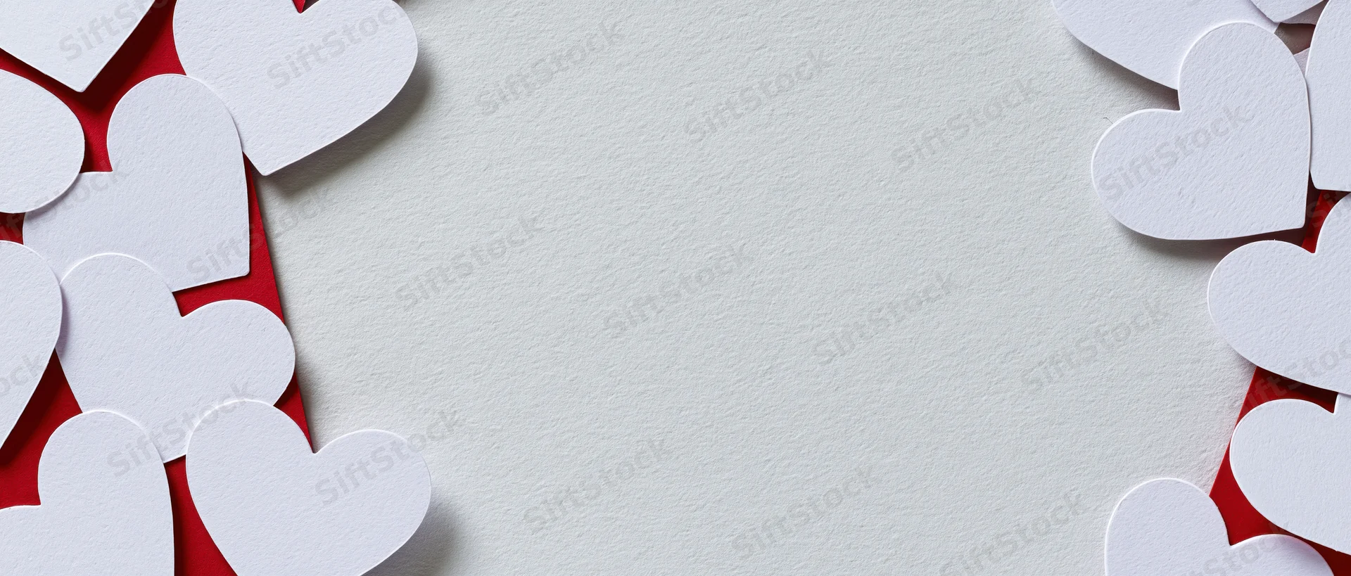 White paper heart cutouts arranged on red and white textured surface with central copyspace