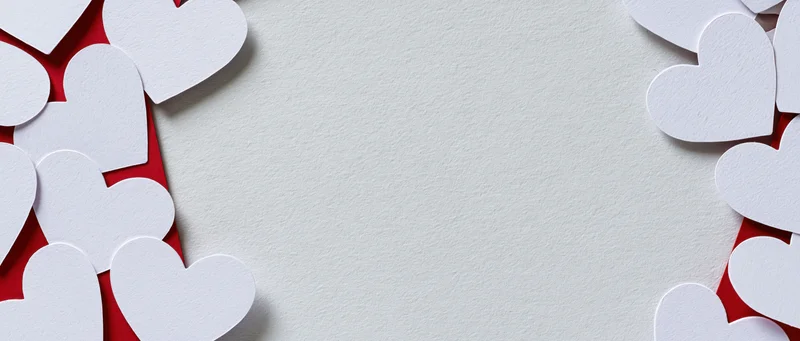 White paper heart cutouts arranged on red and white textured surface with central copyspace