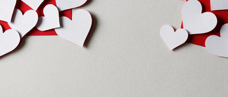White paper heart cutouts scattered across a textured surface with red accents and central copyspace