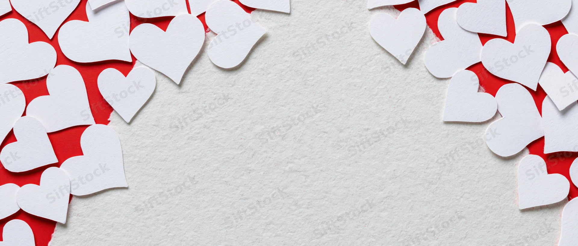 White paper heart cutouts scattered on red and white textured surface forming frame with central copyspace