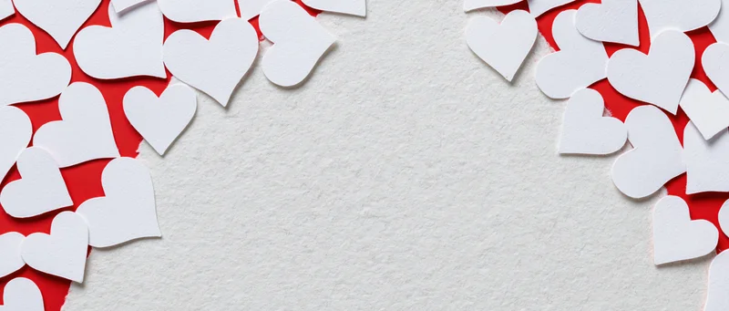 White paper heart cutouts scattered on red and white textured surface forming frame with central copyspace