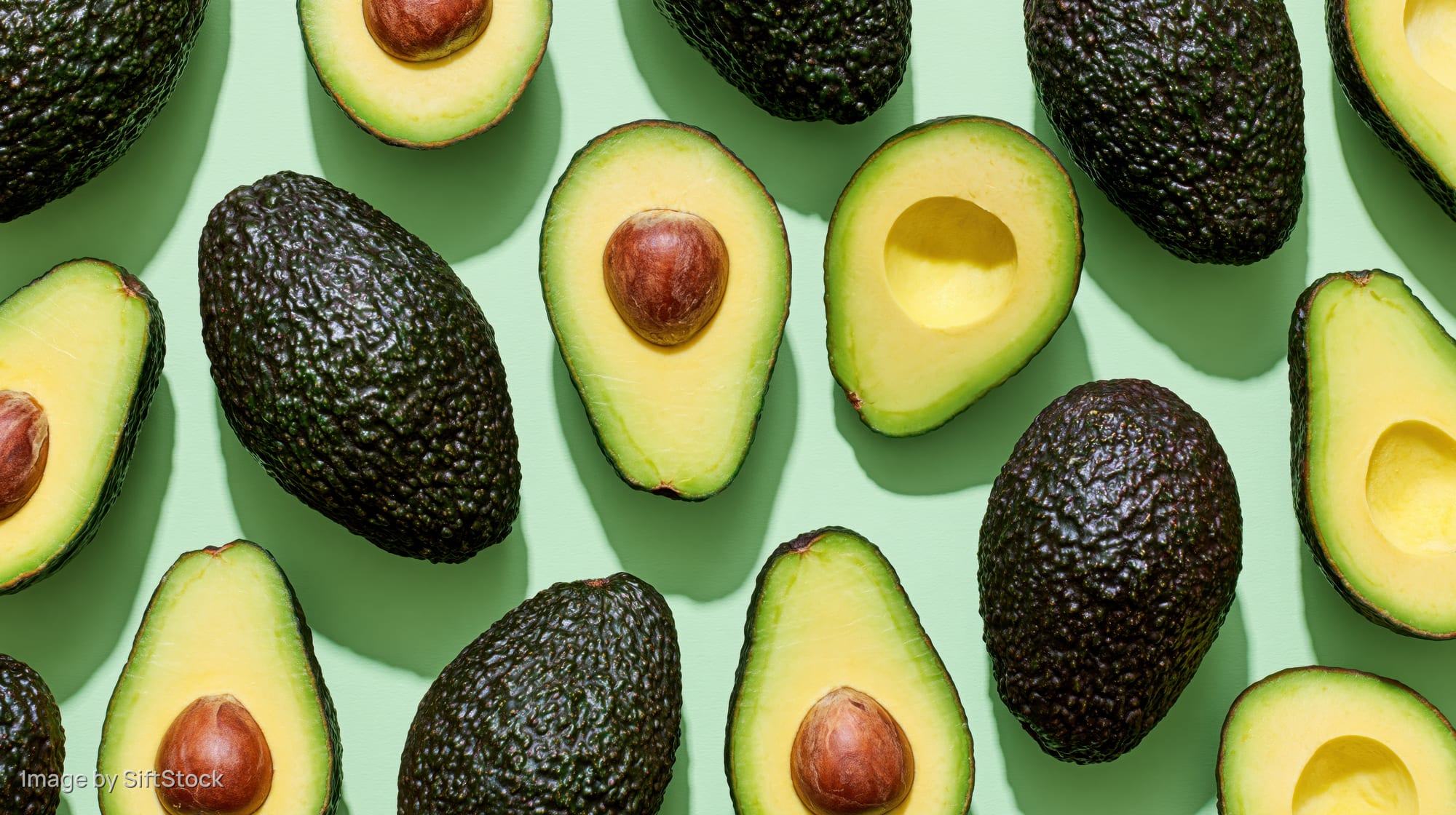 Whole and halved avocados arranged in a flat lay on a green surface