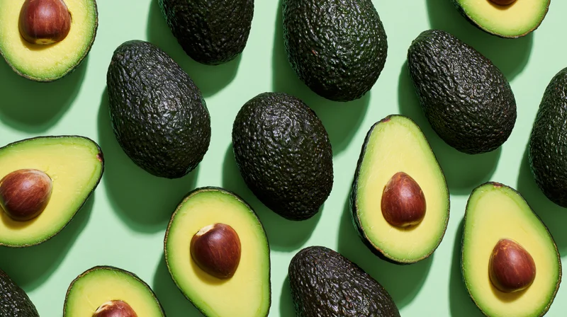 Whole and halved avocados arranged in a scattered flat lay on a green background