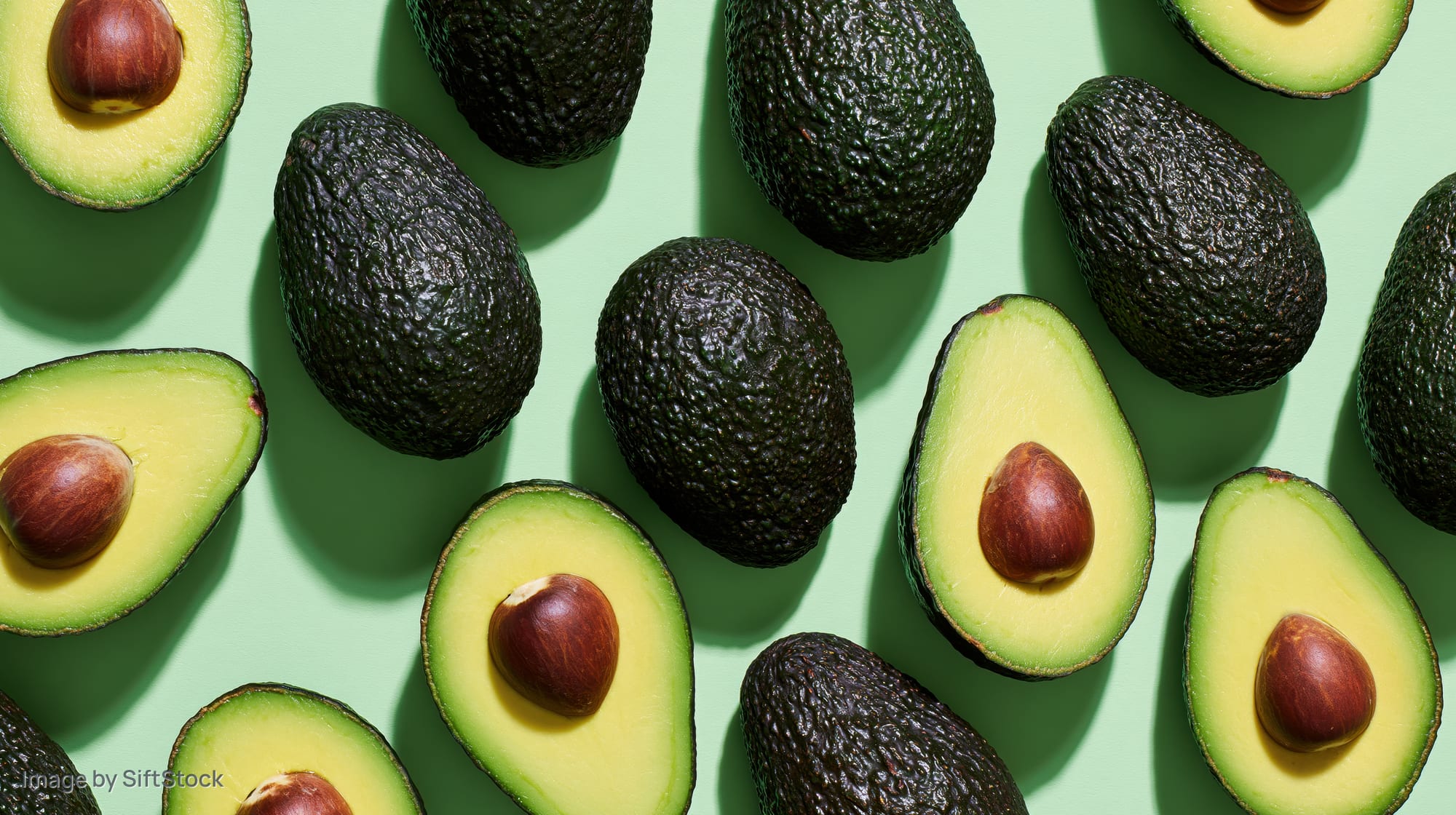 Whole and halved avocados arranged in a scattered flat lay on a green background