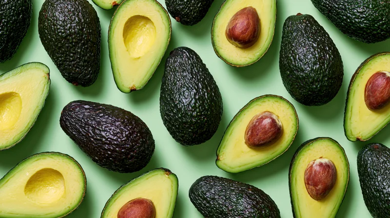 Whole and halved avocados scattered in a flat lay on a green surface
