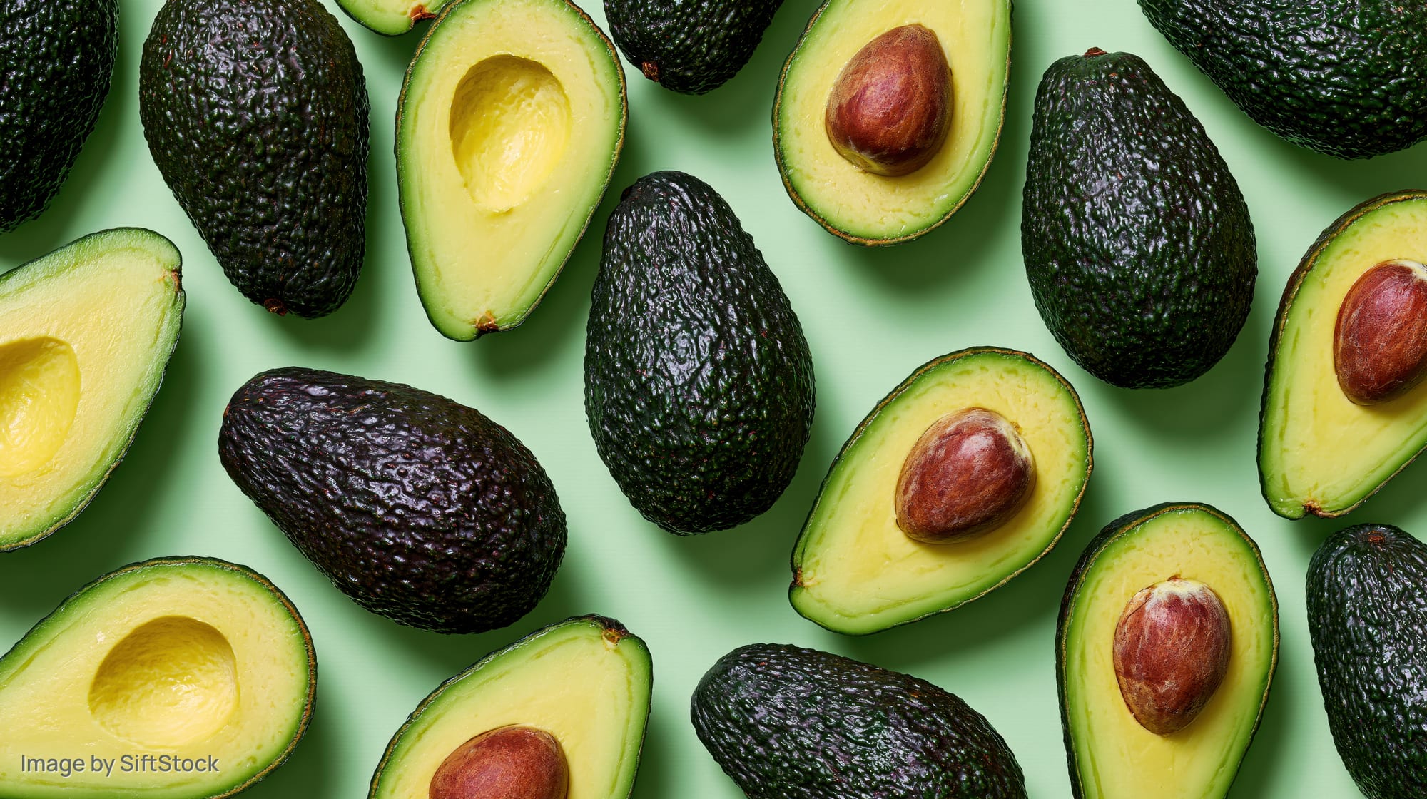 Whole and halved avocados scattered in a flat lay on a green surface