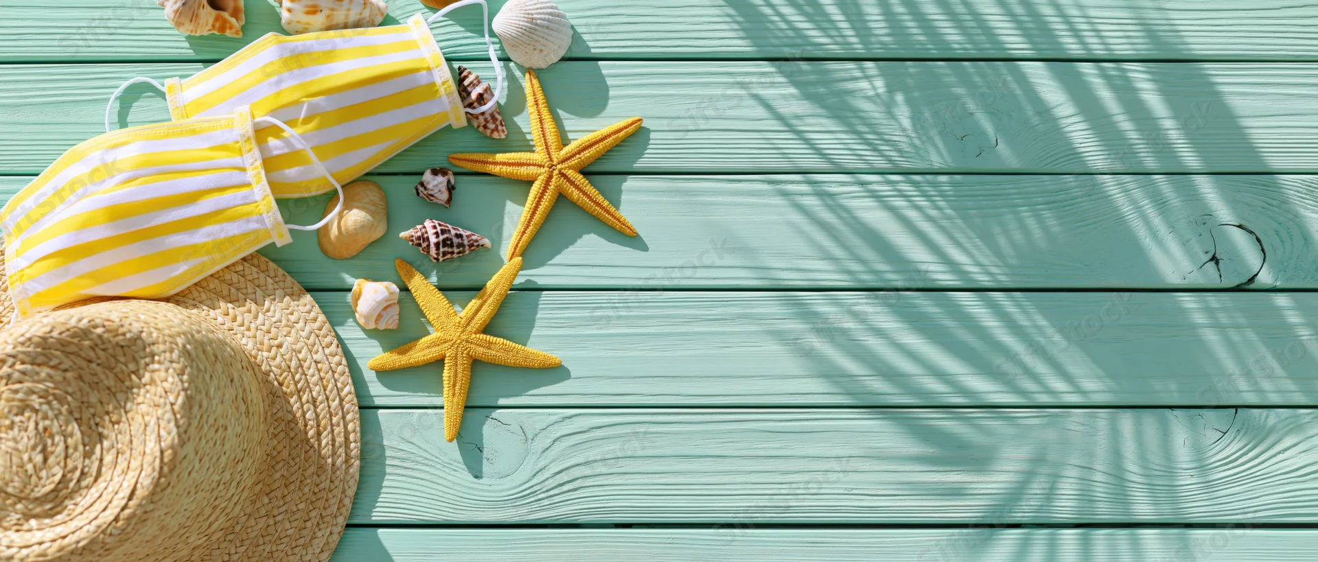 Yellow and white striped face masks with starfish and seashells on a turquoise wooden deck, flat lay top view