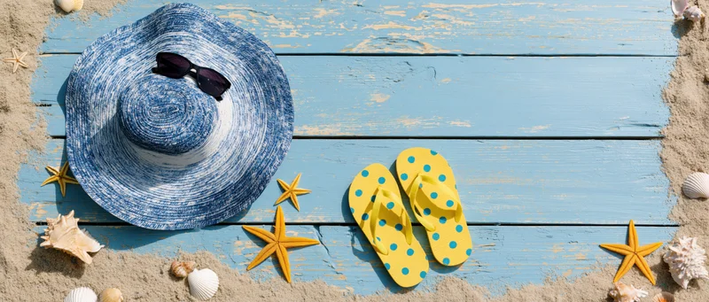 Summer beach accessories arranged on blue wooden planks with sand and shells