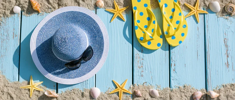 Summer beach accessories arranged on blue wooden deck with sand and shells