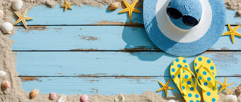 Summer beach accessories arranged on blue wooden planks with sand and shells, overhead view