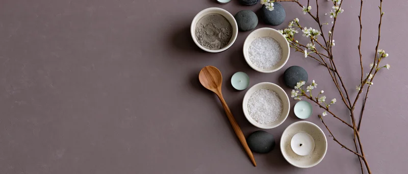 Spa arrangement with bowls of salt, powder, candles, stones and blossoms on muted mauve surface