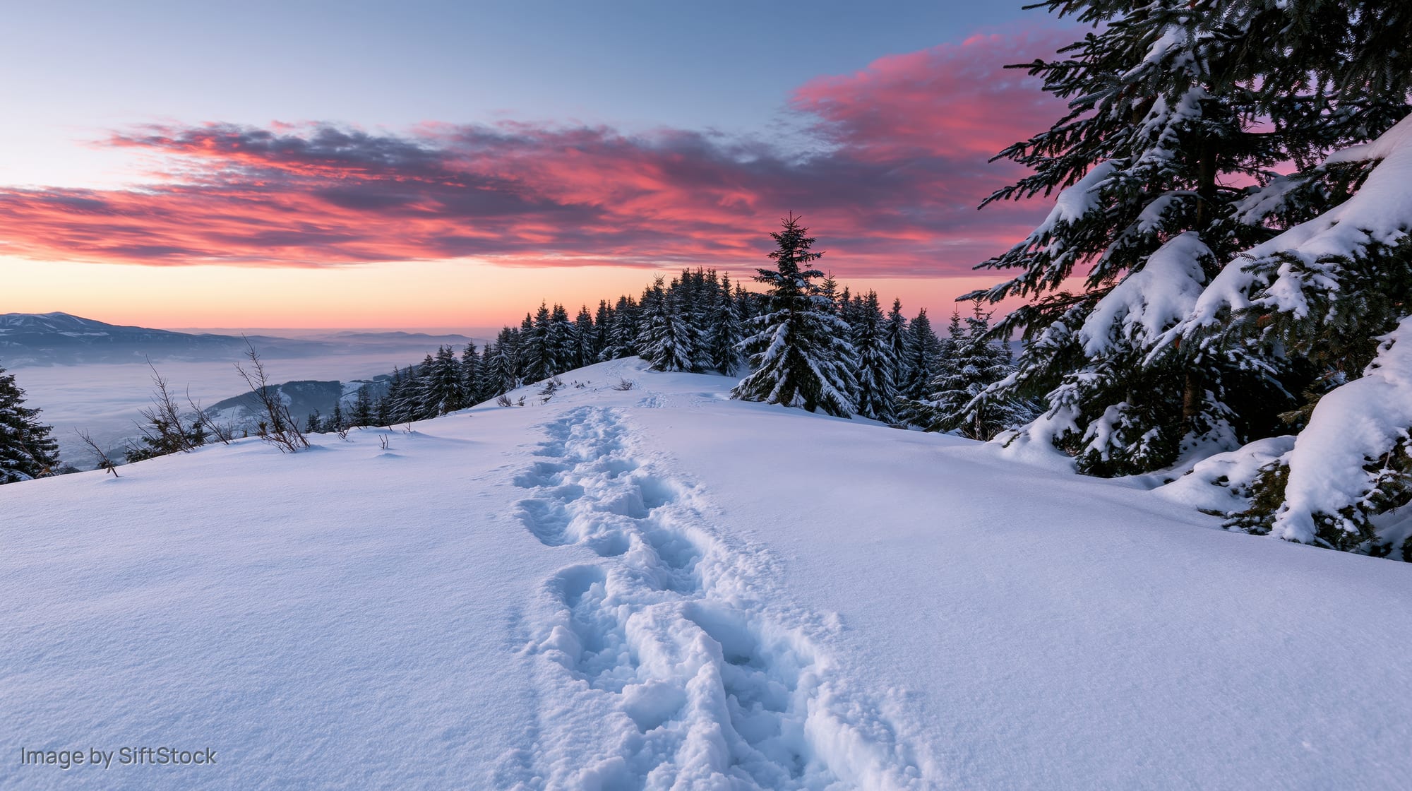 Footsteps in deep snow leading toward a mountain ridge at sunset