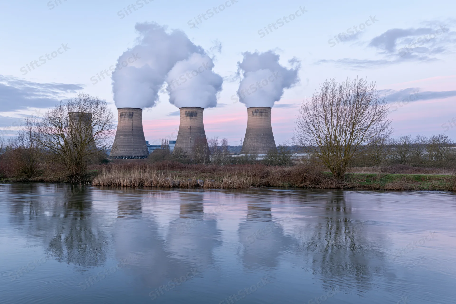 Nuclear cooling towers releasing steam over a river at twilight
