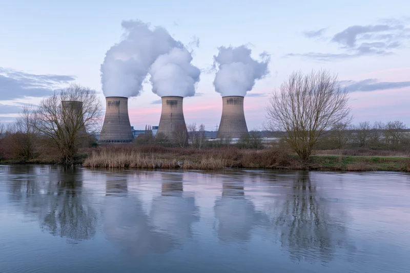 Nuclear cooling towers releasing steam over a river at twilight