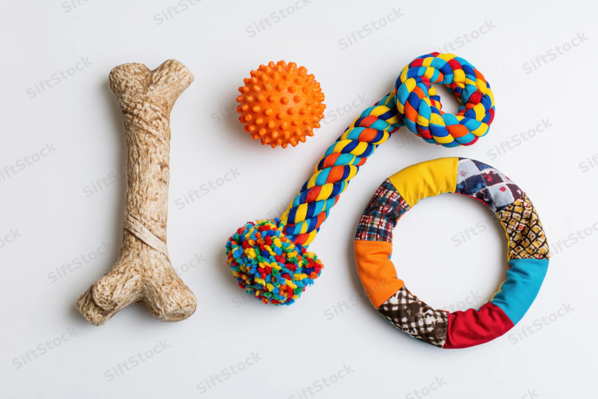 Four dog toys arranged flat lay on white surface including bone, spiky ball, braided rope and patchwork ring