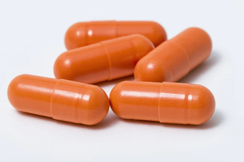 Orange gelatin capsules scattered on a white surface