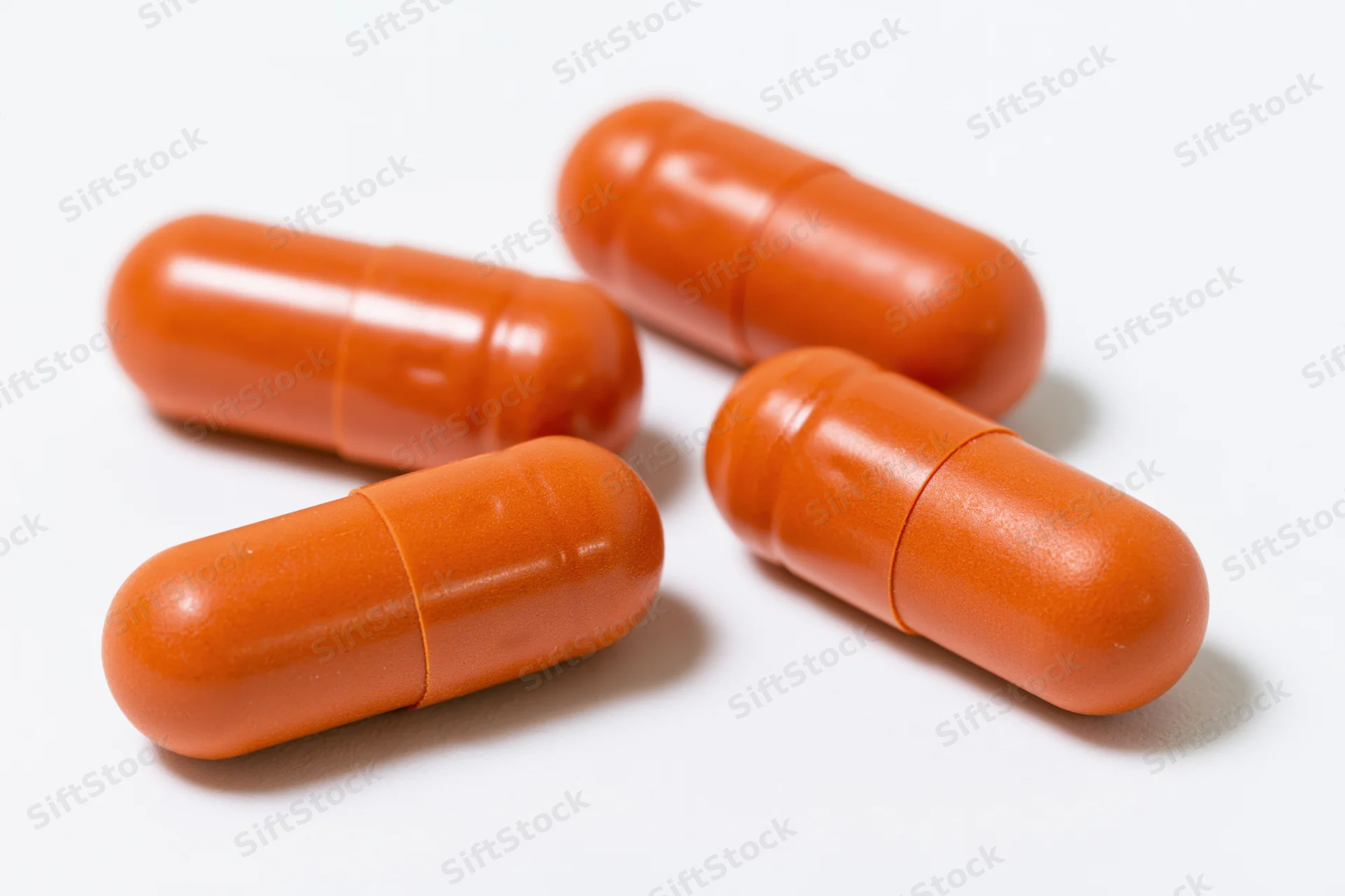 Four orange gelatin capsules scattered on a white surface