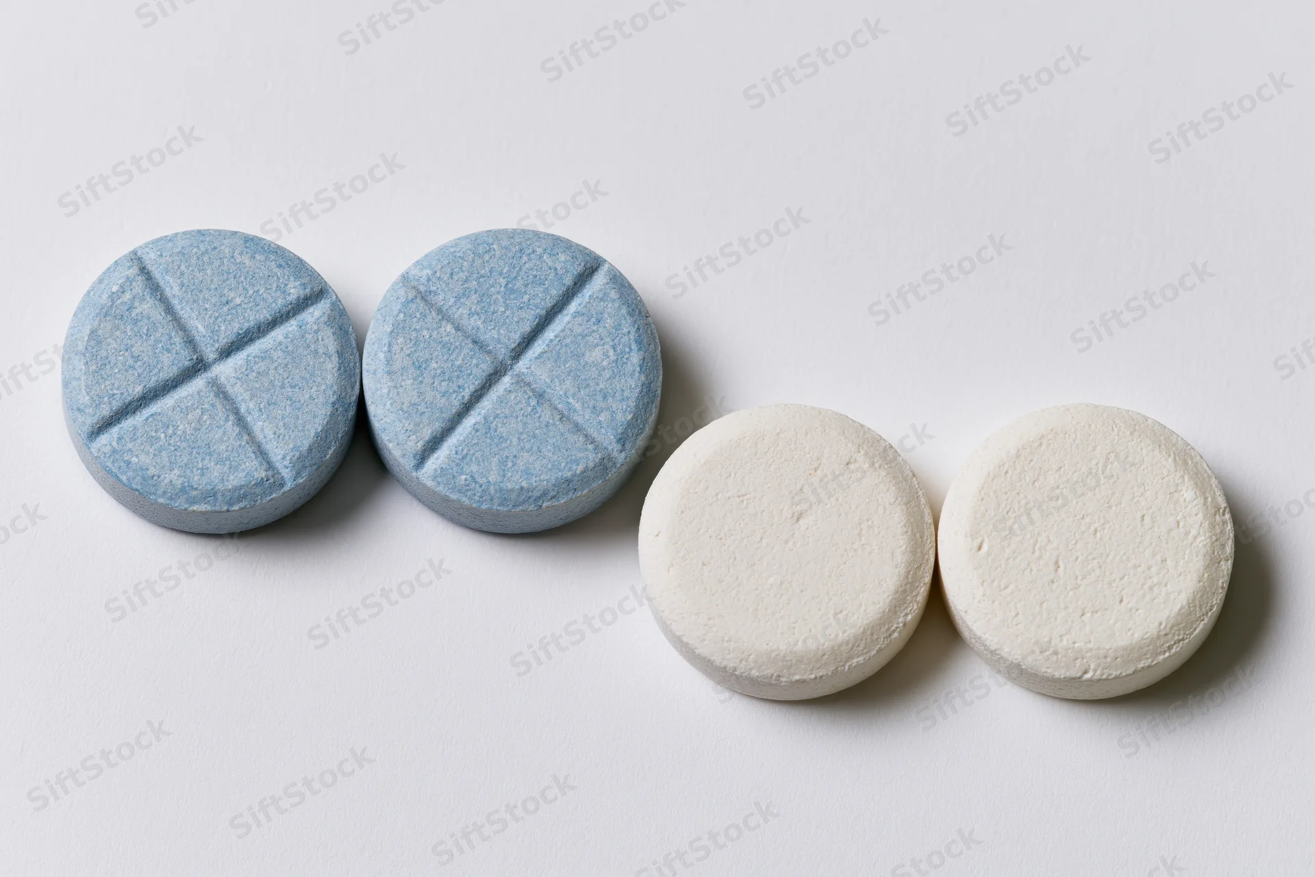 Four round pharmaceutical tablets arranged in two-by-two grid on white surface