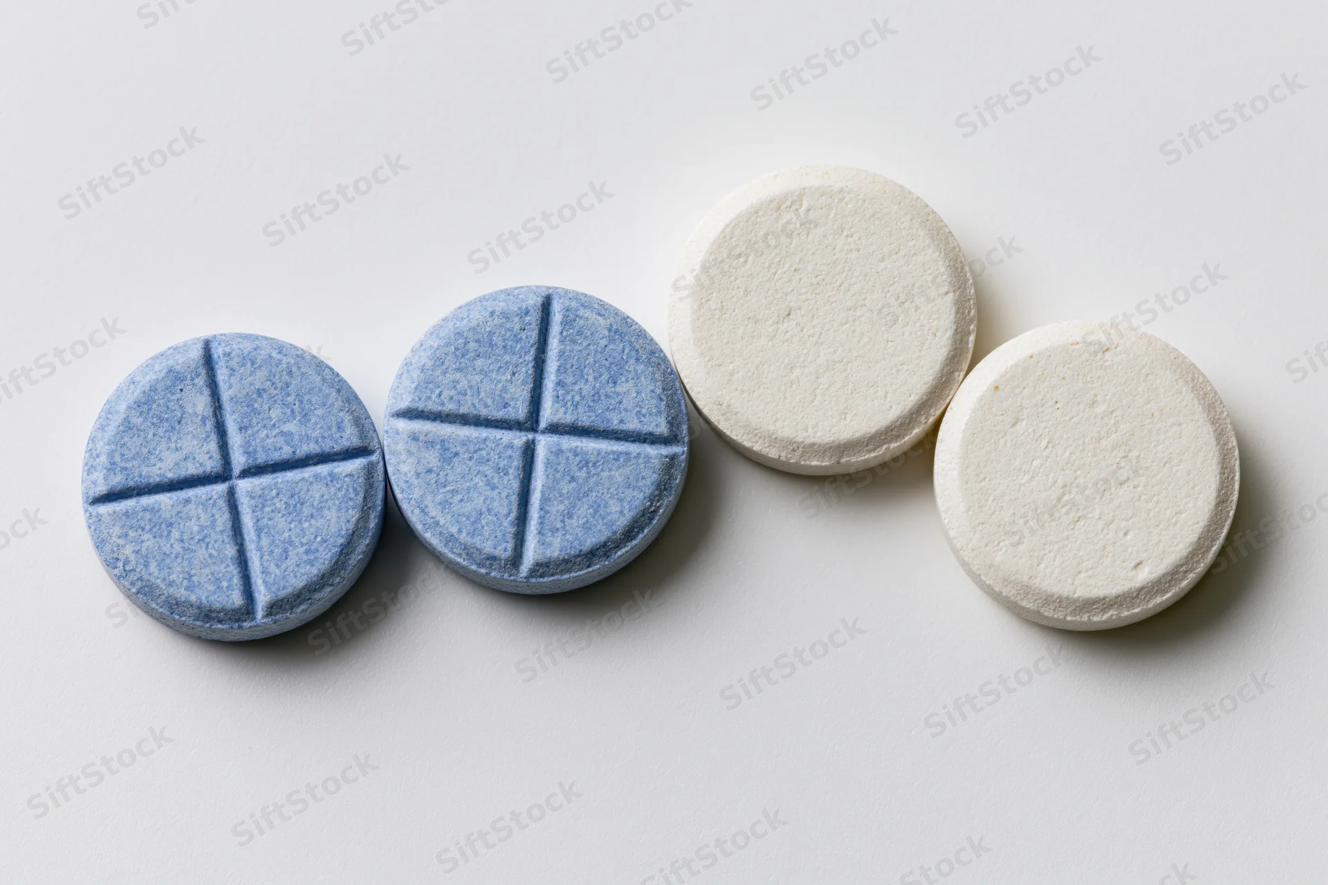 Four round pharmaceutical tablets arranged in a two-by-two grid on a white surface