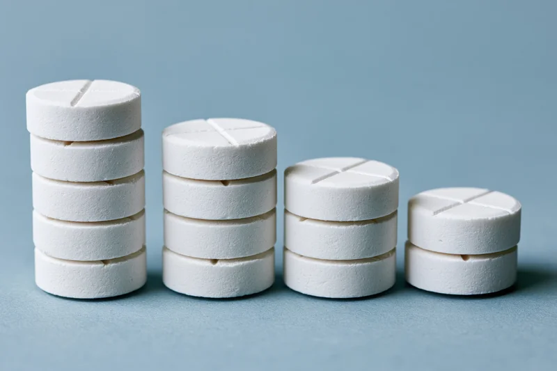 Four stacks of white round scored tablets arranged in descending order on a blue surface