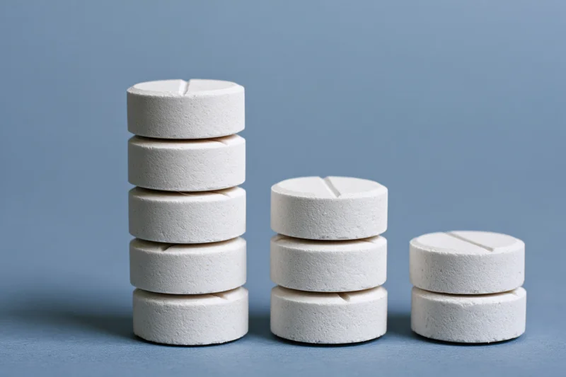 Four stacks of white round scored tablets arranged in descending height on a blue surface