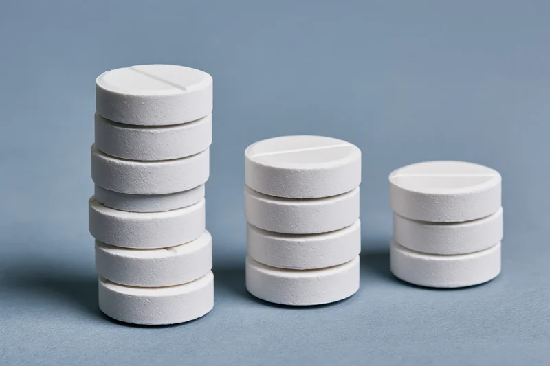 Three stacks of white round scored tablets arranged in descending height on a blue surface