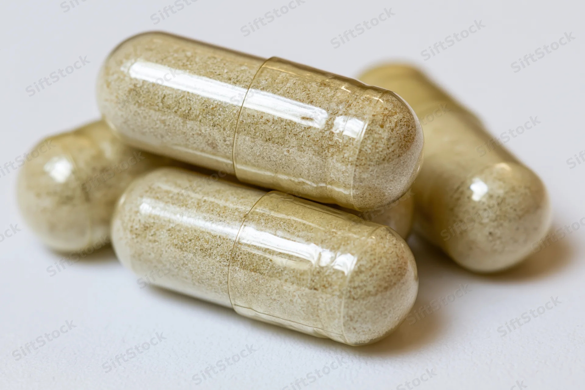 Translucent gelatin supplement capsules filled with fine powder stacked on white surface