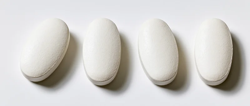 Four white oval pharmaceutical tablets arranged in a horizontal row on a plain white surface