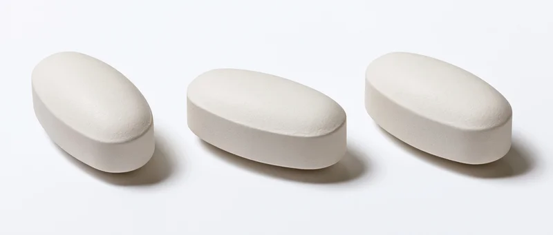 Three white oval pharmaceutical tablets arranged horizontally on a plain white surface