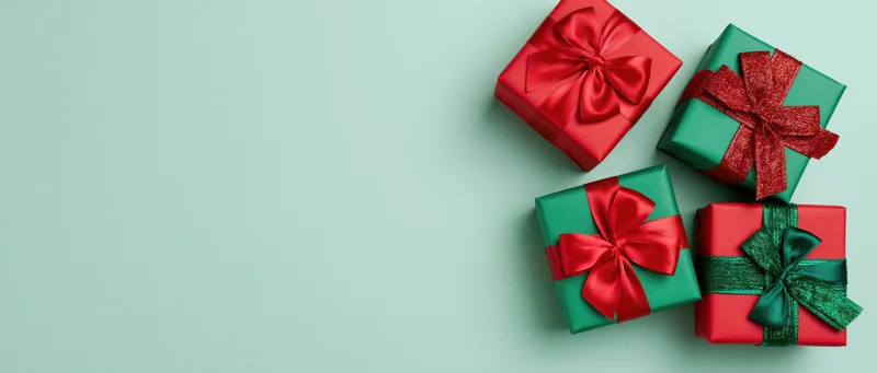 Four wrapped gift boxes in red and green paper with satin ribbons on a light green background