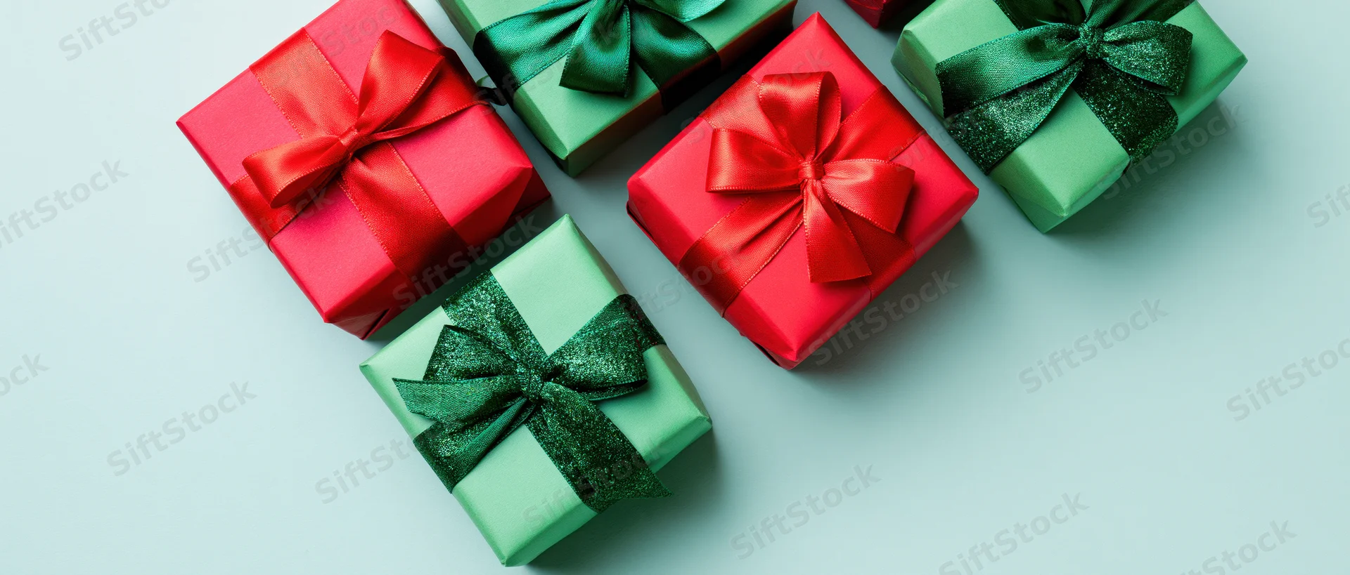Red and green gift boxes with satin bows arranged on a light blue surface