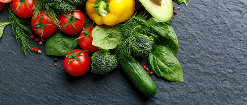 Fresh vegetables and herbs arranged in the upper-left corner on a dark slate surface