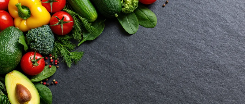 Fresh vegetables and herbs arranged in the upper-left corner on a dark slate surface