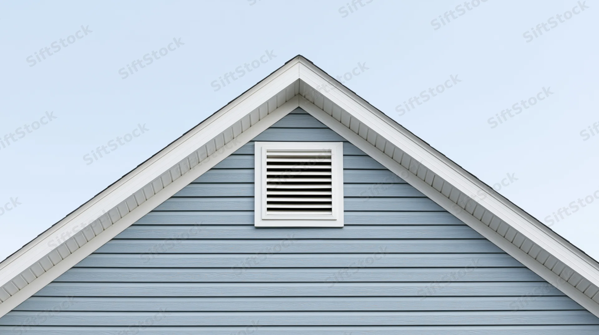 Gable end of a residential house with a louvered attic vent against a clear sky
