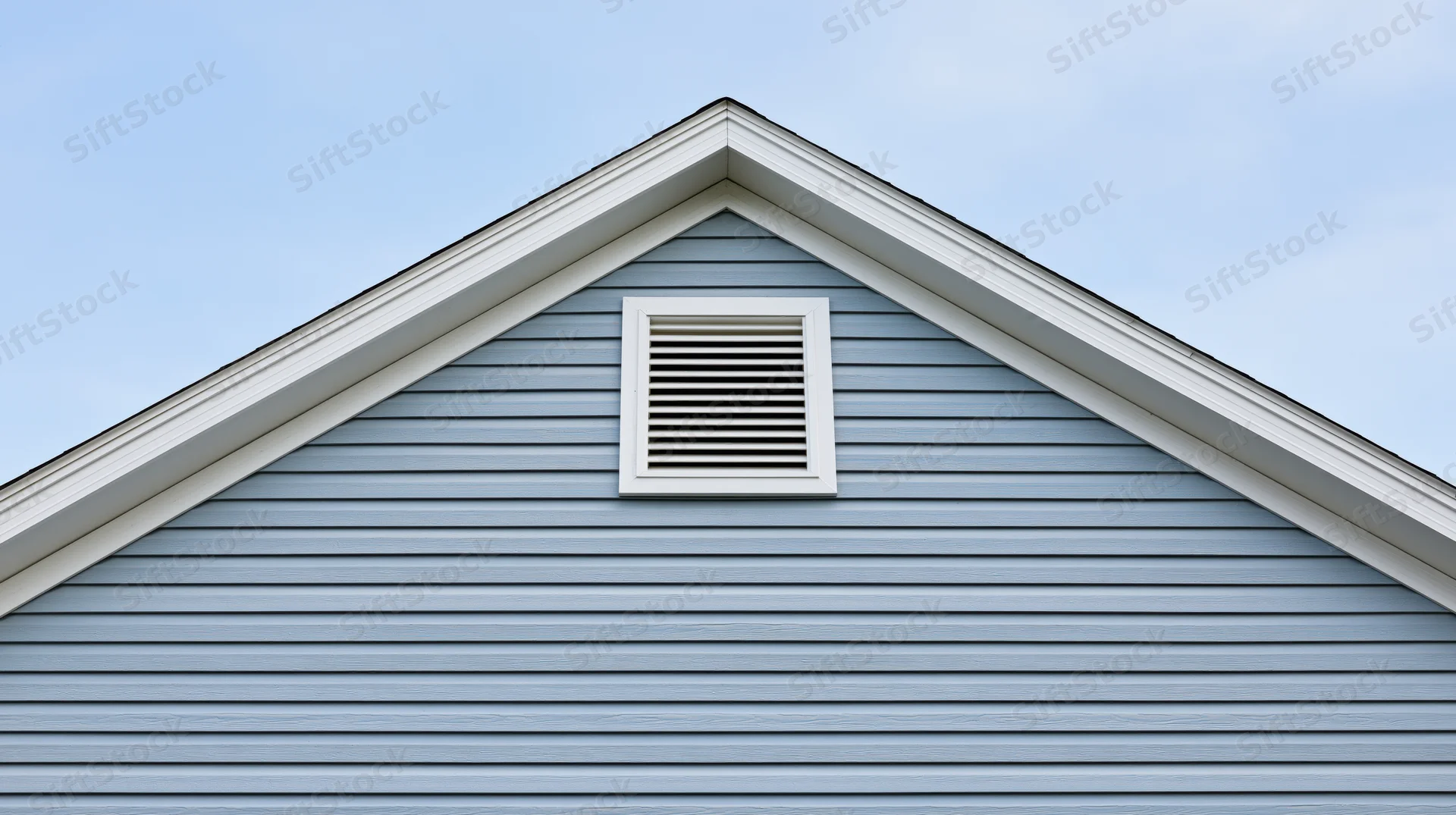 Gable end of a residential house with a louvered attic vent against a blue sky