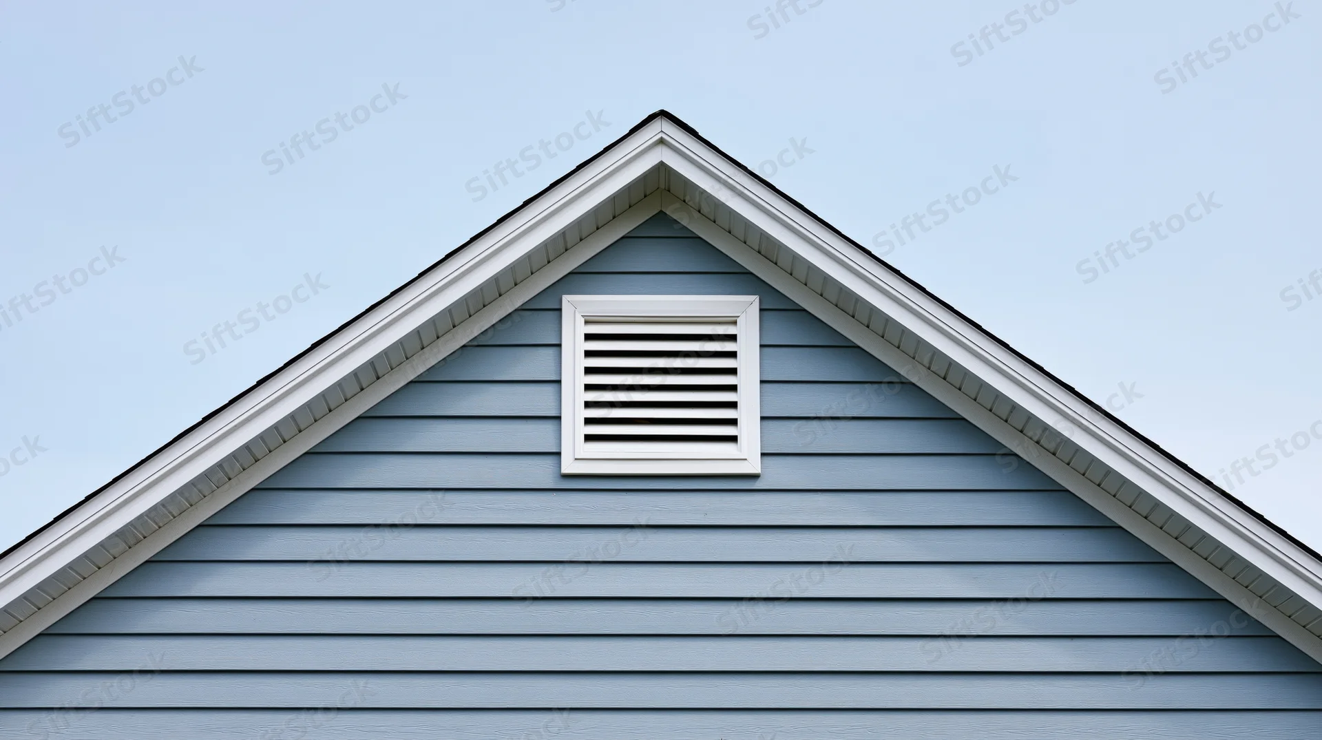 Gable end of a residential house with a louvered attic vent against a clear sky